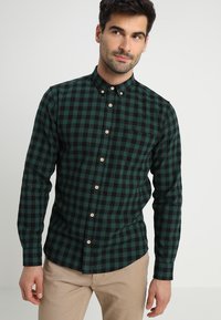 Grøn- og sortternet skjorte med knapper, lange ærmer, spidse kraver, med brune knapper og brystlomme. Blød stoftekstur.