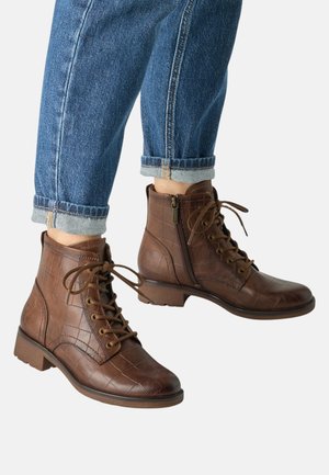 Brune læderstøvler med snørebånd og lynlåse i siden, båret med opbukket blå denimjeans, vist på lys baggrund.