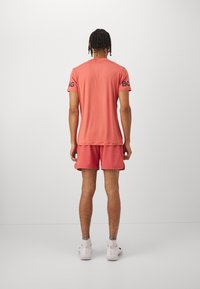 Korallfärgad tränings t-shirt och shorts-set, med korta ärmar och en avslappnad passform. Inkluderar svart text på ärmarna och en mjuk, lätt textur.
