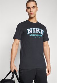 Juodas medvilninis marškinėlis su ryškiu mėlynu ir rožiniu "NIKE ATHLETIC DEPT." grafiniu spaudiniu, apvaliu kaklu ir trumpomis rankovėmis.