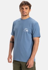 Lichtblauwe katoenen t-shirt met korte mouwen, voorzien van een kleine witte grafische afbeelding van een golf op de linkerkant van de borst. Klassiek ronde halsontwerp.