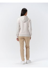 Lichtbeige hoodie van zachte stof, met ribgebreide manchetten en een zak aan de voorkant, gecombineerd met beige broek en witte sneakers.