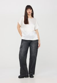 Top bianco fluido a maniche corte abbinato a pantaloni cargo grigio scuro. I pantaloni presentano tasche laterali e una silhouette rilassata a gamba larga.