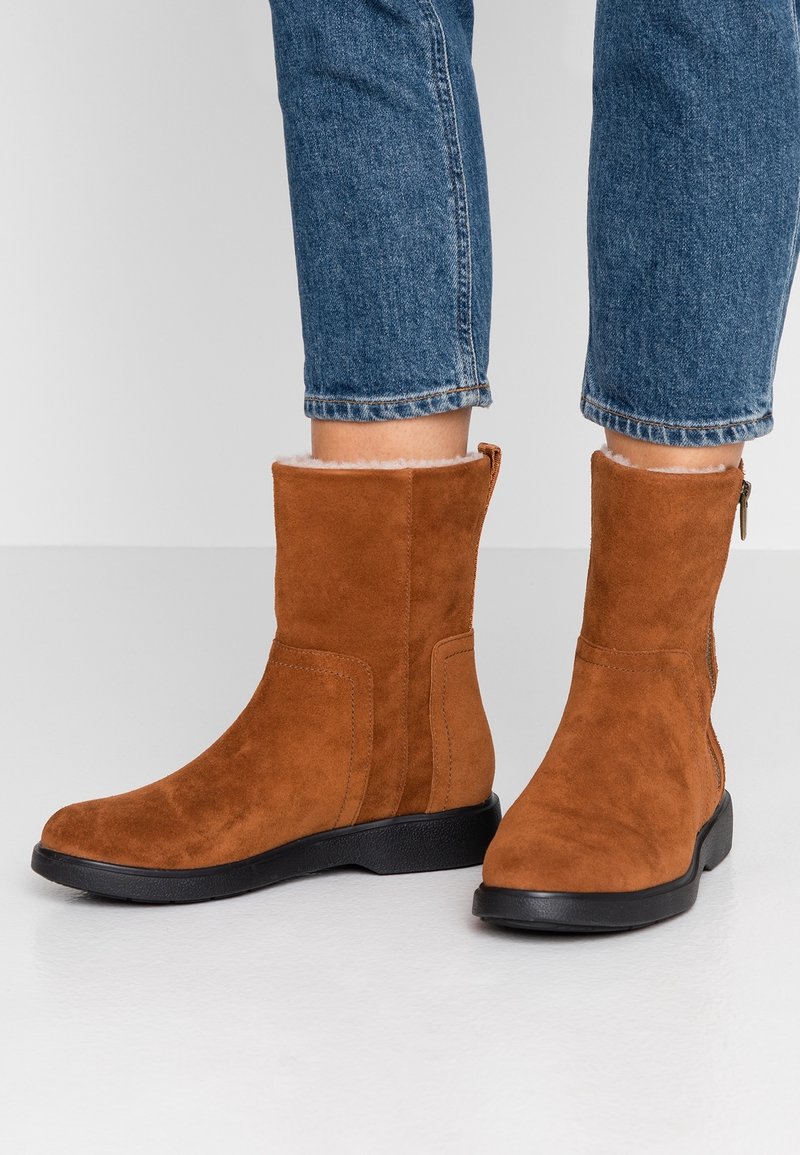 Heren bruine suède enkellaarsjes met een zwarte rubberen zool, gekenmerkt door een gladde textuur en een zijrits voor gemakkelijk aan- en uittrekken. Voering van zacht materiaal.