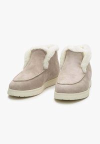 Beige suède enkelaarsen met witte nepbont voering, ronde neus en platte rubberen zolen. Stiksels langs de bovenrand.