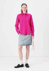 Fuchsia long-sleeve button-up shirt, light blue denim skirt with white lettering, black loafers, and a small pale pink handbag.