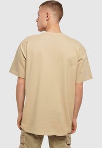 Beige bomulds t-shirt med afslappet pasform, korte ærmer og rund hals. Bagfra ses en glat tekstur og et minimalistisk design.