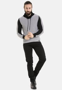 Schwarzer und weißer Kapuzenpullover mit strukturierten Mustern, langen Ärmeln und lockerer Passform, kombiniert mit schwarzen Hosen und schwarzen Stiefeln.
