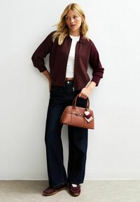 Burgundy cropped cardigan, white t-shirt, dark flared jeans, brown leather handbag with heart keychain, and brown athletic shoes.