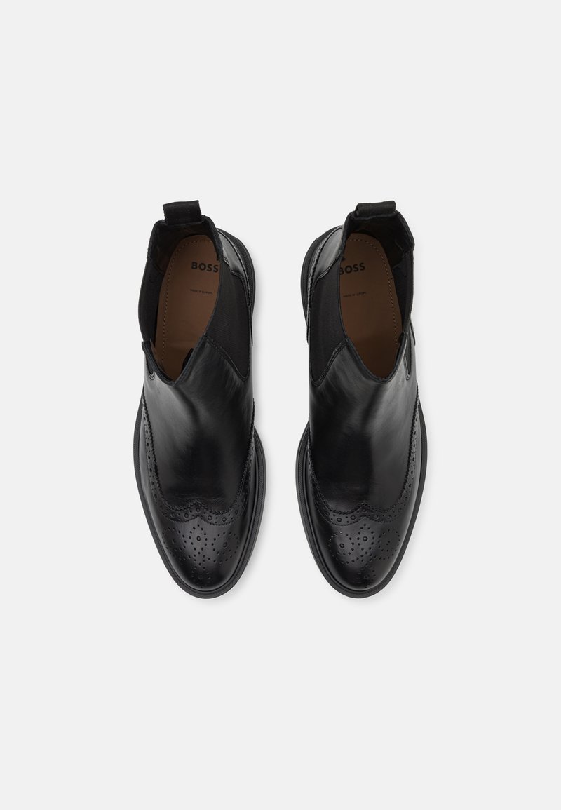 Schwarze Lederstiefeletten mit elastischen Seiteneinsätzen, Broguemuster und glatter Oberfläche. Entworfen mit einer abgerundeten Spitze und strukturierten Sohlen.