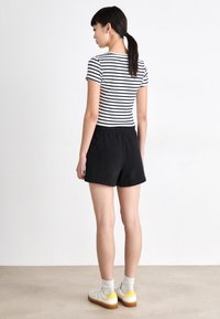 Sorte bomullsshorts med elastisk midje sammen med en svart og hvit stripete tettsittende t-skjorte. Brukt med hvite sko med gule detaljer.