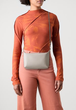 Gray crossbody bag with a smooth texture, rectangular shape, and adjustable strap; worn over a rust-colored long-sleeve top and pink pants.