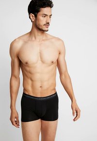 Fekete boxeralsók testhez simuló szabással és puha anyagból, kontrasztos szürke derékpánttal, amelyen a márkanév látható.
