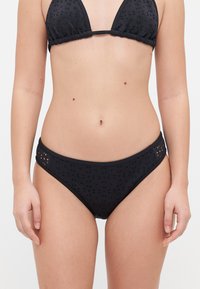 Ensemble de bikini noir comprenant un haut triangulaire avec des bords froncés et un bas assorti. Le tissu présente un motif texturé subtil avec des détails découpés.