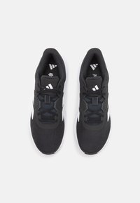 Baskets de sport noires avec une tige en maille respirante, un design à lacets, un col rembourré et des accents blancs sur la semelle et le côté.