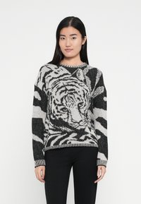 Strickpullover mit schwarz-weißem Tiger-Muster, rundem Ausschnitt und geripptem Saum. Weiche Textur und lockere Passform.