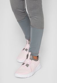 Chaussures de sport roses avec tige en maille, accents gris et semelle blanche. Portées avec des leggings gris ayant des panneaux contrastants et une coupe ajustée.