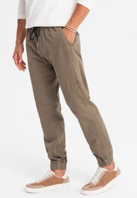 Olijfgroene joggerbroeken met elastische boorden en zijzakken, gemaakt van lichtgewicht materiaal. Gecombineerd met beige en witte sneakers.