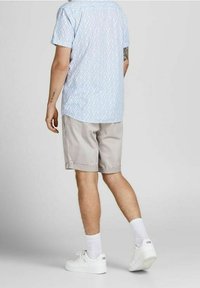 Košile s krátkým rukávem modré barvy s geometrickým vzorem, spárovaná se světle šedými šortkami, bílými teniskami a bílými ponožkami. Zobrazeno zezadu.