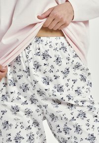 Kwiatowe spodnie piżamowe w białym kolorze z granatowymi i szarymi kwiatami; elastyczny pas; zestawione z jasnoróżową bluzką z długim rękawem.