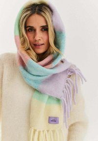 Kobieta nosząca pastelowy szalik w paski z frędzlami owinięty wokół głowy i szyi, w połączeniu z kremowym, puszystym sweterkiem.