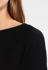 Schwarzer Pullover mit weitem Ausschnitt, geripptem Textur an den Ärmeln und einem glatten Körper. Weiches Strickmaterial mit minimalen Design-Details.