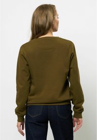 Olivno zelena majica s okruglim izrezom, rebrastim manžetama i glatkom teksturom, u kombinaciji s tamnim trapericama. Stražnji pogled prikazuje detalje na ramenima.