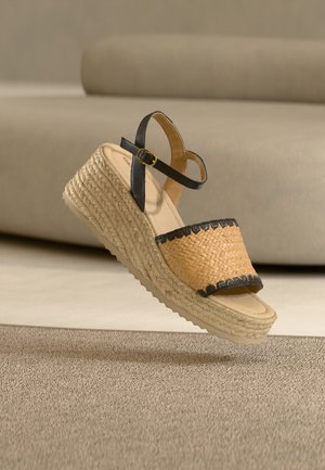 Πλεγμένο σανδάλι πλατφόρμας από άχυρο με μαύρο δερμάτινο λουράκι στον αστράγαλο και διακοσμητικές λεπτομέρειες. Ελαφρύ σχέδιο με υφή σόλας από τζούτ. Παλέτα χρωμάτων: καφέ και μαύρο.