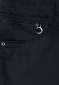 Gros plan d'une poche de pantalon en tissu sombre avec une fermeture éclair horizontale et un tirette métallique circulaire.