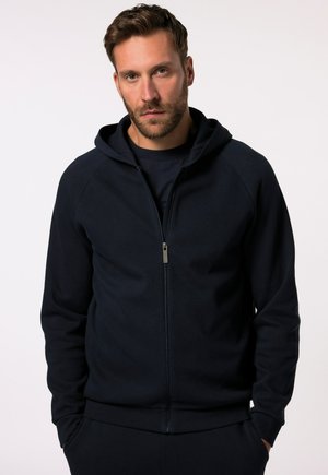 Felpa con zip di colore blu navy, con finitura testurizzata, maniche raglan e zip frontale. Presenta un cappuccio e una vestibilità comoda e rilassata.