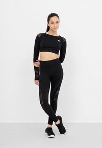 Sort atletisk crop top og tights med mesh-detaljer og afrundet kant. Har et logo på toppen; tætsiddende design med strækbart stof.