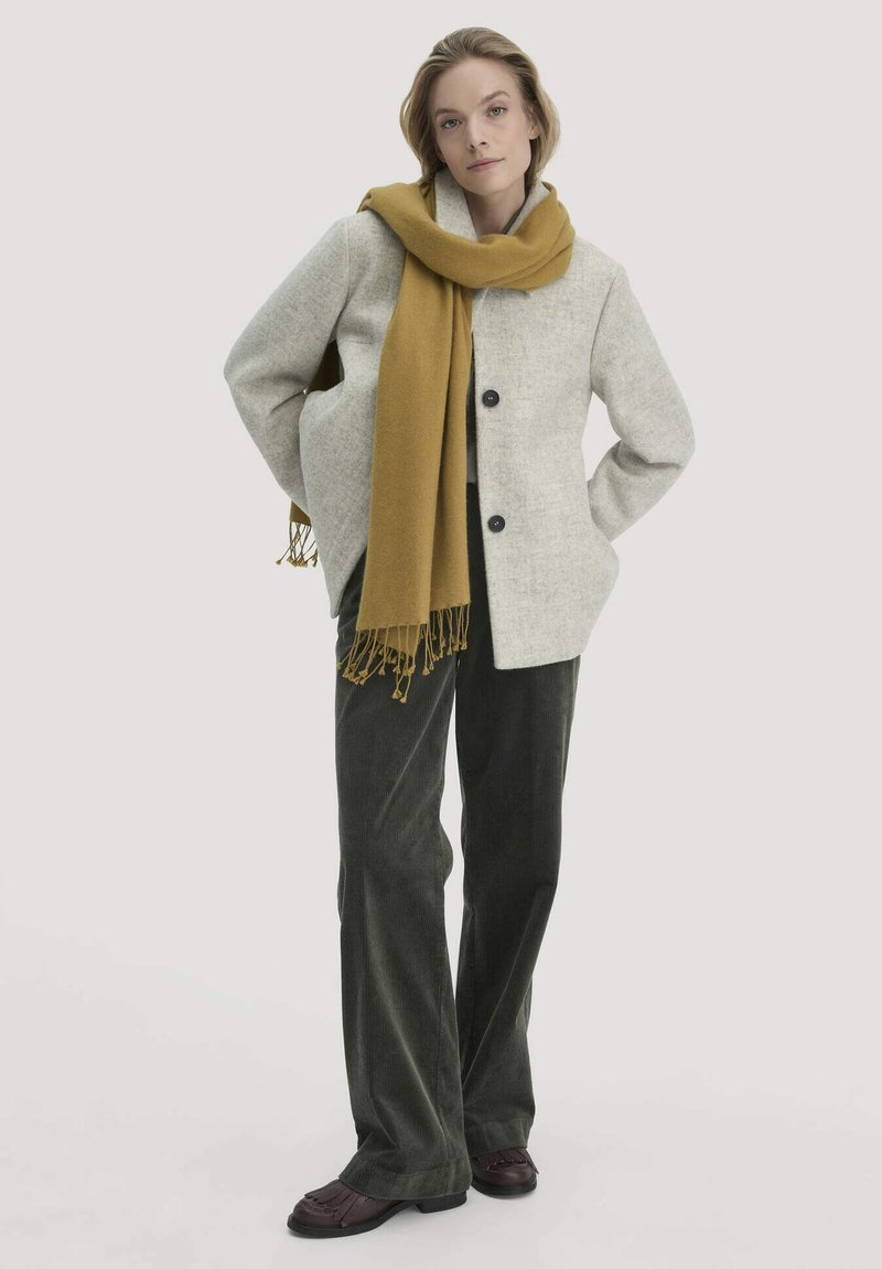 Grijze wolmix jas met zwarte knopen, mosterdkleurige sjaal met franjes, groene corduroybroek en donkerbruine loafers. Eenvoudig, op maat gemaakt ontwerp.