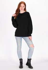 Felpa nera oversize con maniche lunghe, caratterizzata da un sottile dettaglio logo. Abbinata a jeans skinny azzurri strappati e stivaletti neri.