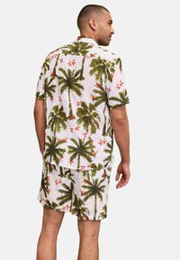 Camicia a maniche corte e pantaloni corti bianchi con motivo di palme verdi e fiori rossi; tessuto leggero; vestibilità casual e rilassata.