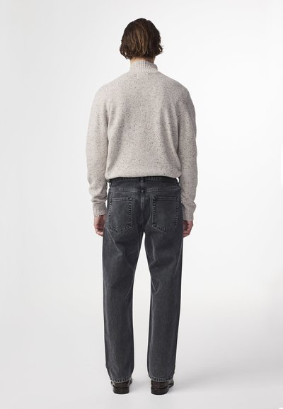 Maglione grigio chiaro a maglia maculata con collo a costine, abbinato a jeans grigio scuro a taglio morbido con due tasche posteriori.