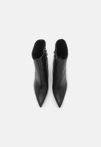 Une paire de bottines noires en cuir à bout pointu avec des fermetures éclair latérales, présentées de dessus sur un fond blanc.
