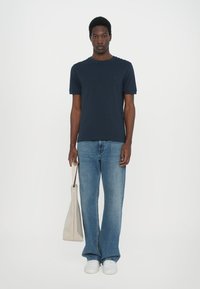 Marineblå bomulls T-skjorte med rund hals, kombinert med lyseblå vide jeans. Holder en lys beige totebag, med hvite sneakers.