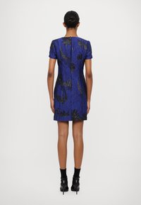 Īsām piedurknēm kleita spilgti zila ar melniem ziedu rakstiem, ar pieguļošu dizainu, teksturētu audumu un taisnu apakšmalu.