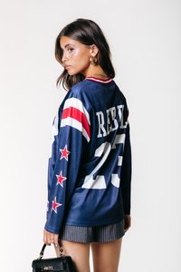 Blå langermet jersey med røde og hvite striper, med "REBEL" og nummer "23" på baksiden, samt stjernedetaljer på ermene.