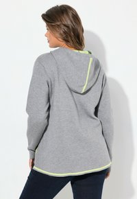 Haut à capuche gris avec une capuche, présentant un accent vert néon le long des coutures. Texture douce, manches longues et coupe décontractée.