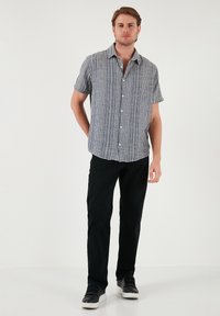 Korte mouwen button-up shirt in grijs met witte verticale strepen, gecombineerd met zwarte broek en zwarte Sneakers. Eenvoudige kraag en klassieke pasvorm.