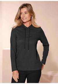 Zwarte hoodie met ribbelstructuur, lange mouwen en verstelbare trekkoorden bij de hals. Gecombineerd met zwarte broek.