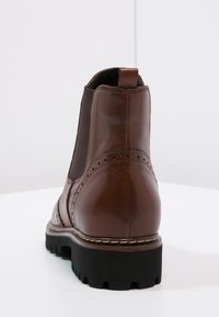 Bottine Chelsea en cuir marron avec des panneaux latéraux élastiques, bout rond, détails brogue et une semelle en caoutchouc noir robuste.