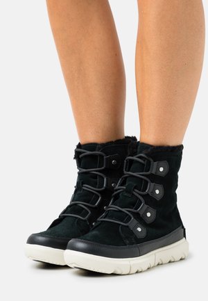 Schwarze Wildleder-Stiefeletten mit Kunstfellfutter, fünf verstellbaren Riemen und einer cremefarbenen Gummisohle. Ausgestattet mit einer gepolsterten Ferse und einer strukturierten Sohle.