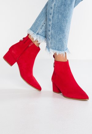 Red suede ankle boots with a pointed toe, block heel, and zipper closure. Fitted style paired with frayed hem blue jeans.