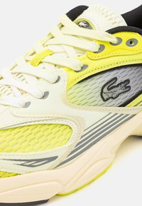 Baskets Lacoste avec une tige en mesh dotée d'accents jaune fluo, de lacets blancs et d'un panneau latéral gris avec un logo de crocodile noir.