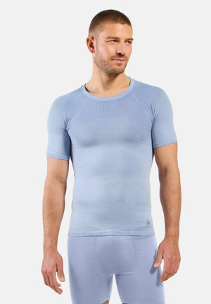 Mann trägt hellblaues, strukturiertes kurzärmeliges Sportshirt und passende Shorts, steht und schaut leicht zur Seite.