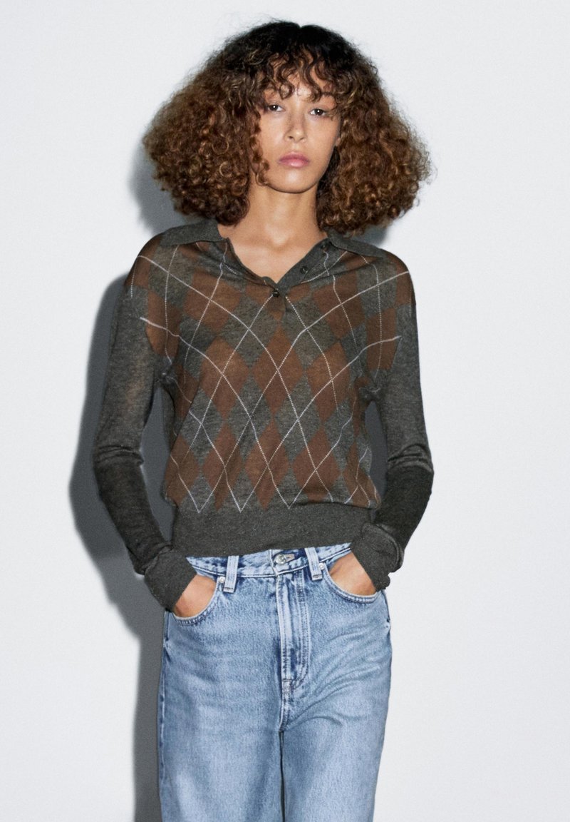 Donkergrijze gebreide pullover met een bruine ruitpatroon, lange mouwen en een kraag. Gecombineerd met lichtblauwe high-waisted jeans.
