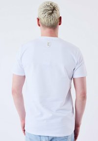 Camiseta blanca de manga corta con cuello redondo y un pequeño logo centrado en la parte superior de la espalda. Textura suave y corte regular.
