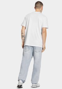 Biała bawełniana koszulka z krótkim rękawem, luźny krój. Noszona z jasnoniebieskimi dżinsami z tylnymi kieszeniami i wyblakłym wyglądem.